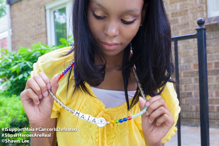 Maia show her necklace, A bead is added for every procedure she has undergone