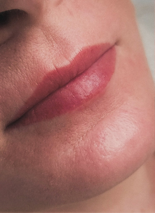 Close-up of a person's lips with soft pink lip tattoo and smooth skin texture.