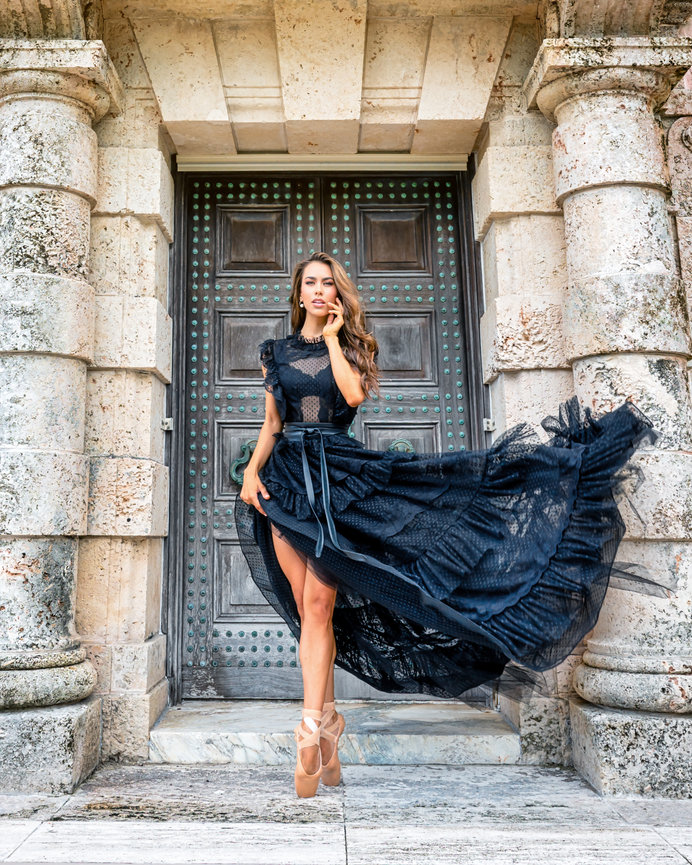 Model in a flowing black dress poses gracefully in front of an ornate stone doorway.