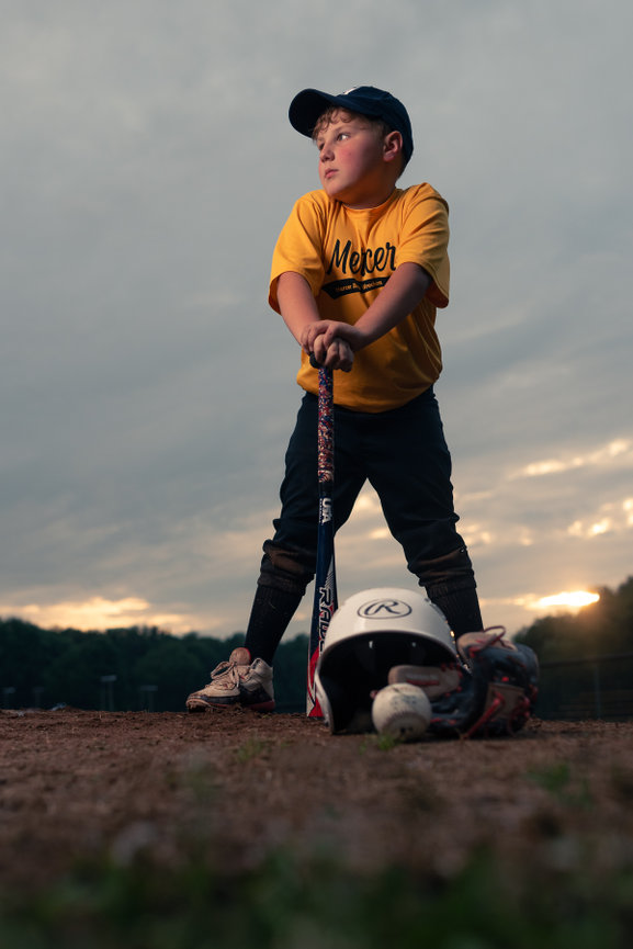 youth baseball player who is leaning on his bat looking away from the camera
