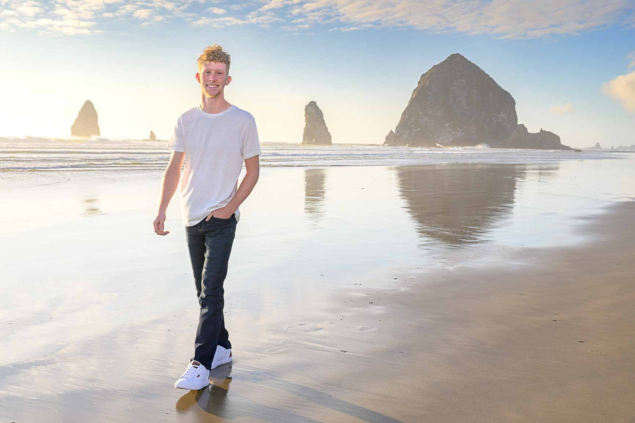 Senior guy walking along the beach with Haystack Rock behind him and a clear blue sky