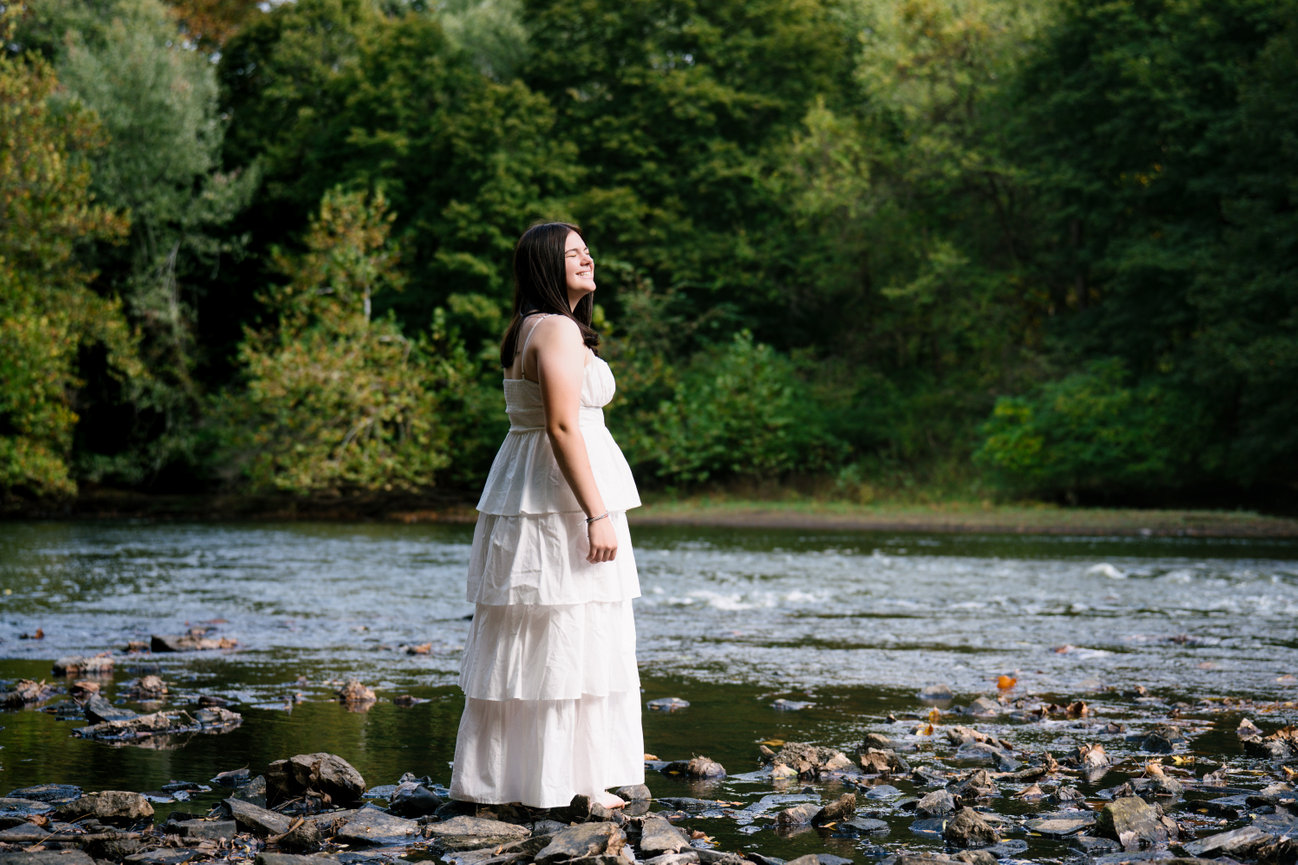 senior girl in a white dress near a river during her senior pictures in sharpsville pa