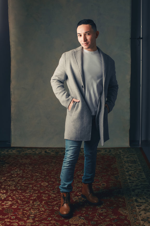In studio with strong male style and lighting with client wearing denim pants and grey coat in a vintage created set design.