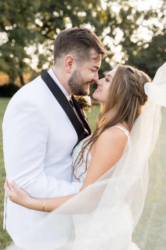 Bride and groom touching noses and smiling at each other while her veil swoops in front