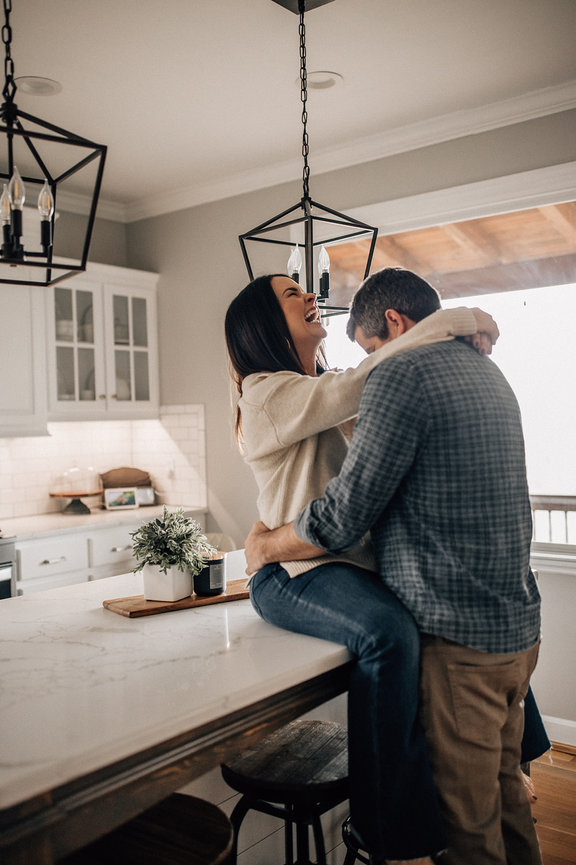 A wife sits on a counter laughing with her husband's arms around her during a Huntsville Alabama family photoshoot