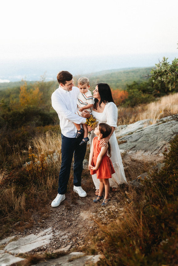 A family with two children standing on top of a rocky ridge in Sussex County, New Jersey at sunset.