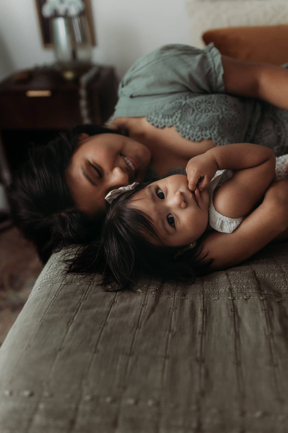A woman in a green dress snuggling with her daughter on a bed during a New Jersey motherhood session.
