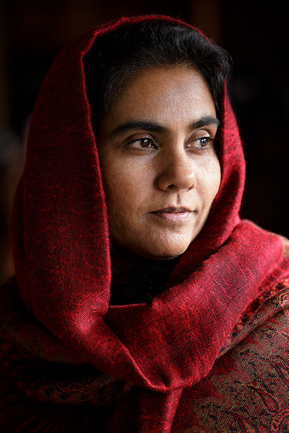 Indoor portrait of a woman wearing a red shawl, captured in soft natural-style light with a calm, contemplative expression and a fine art feel