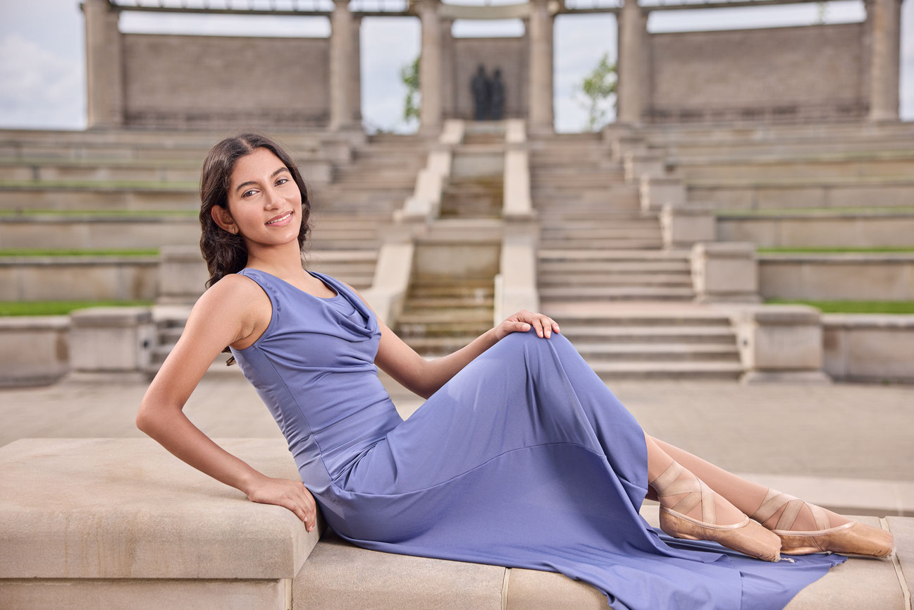 High school senior ballerina reclining gracefully in a blue dress and pointe shoes at the Centerpiece in Coxhall Gardens, photographed by Wahala Portraits.