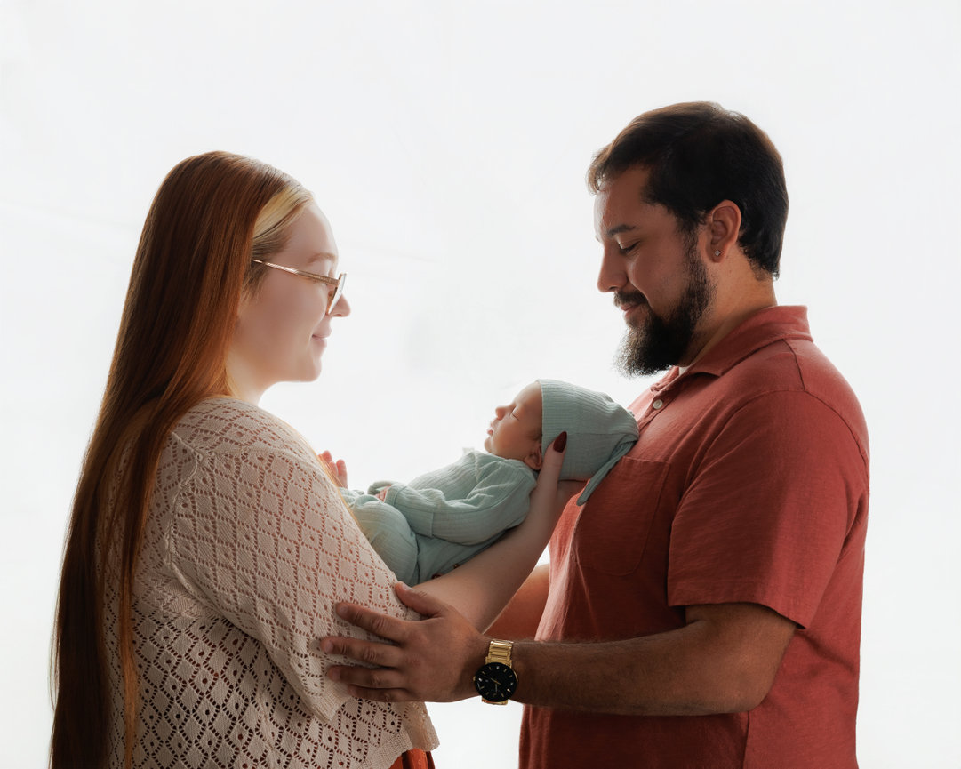 Expectant couple holding a wrapped newborn in soft window light
