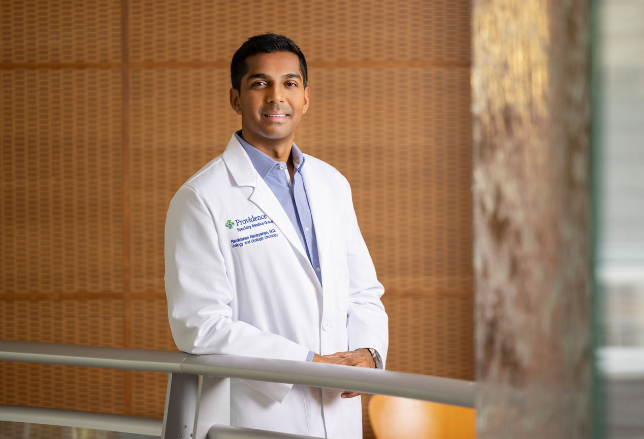 Male doctor in a white coat standing in a modern hospital interior.