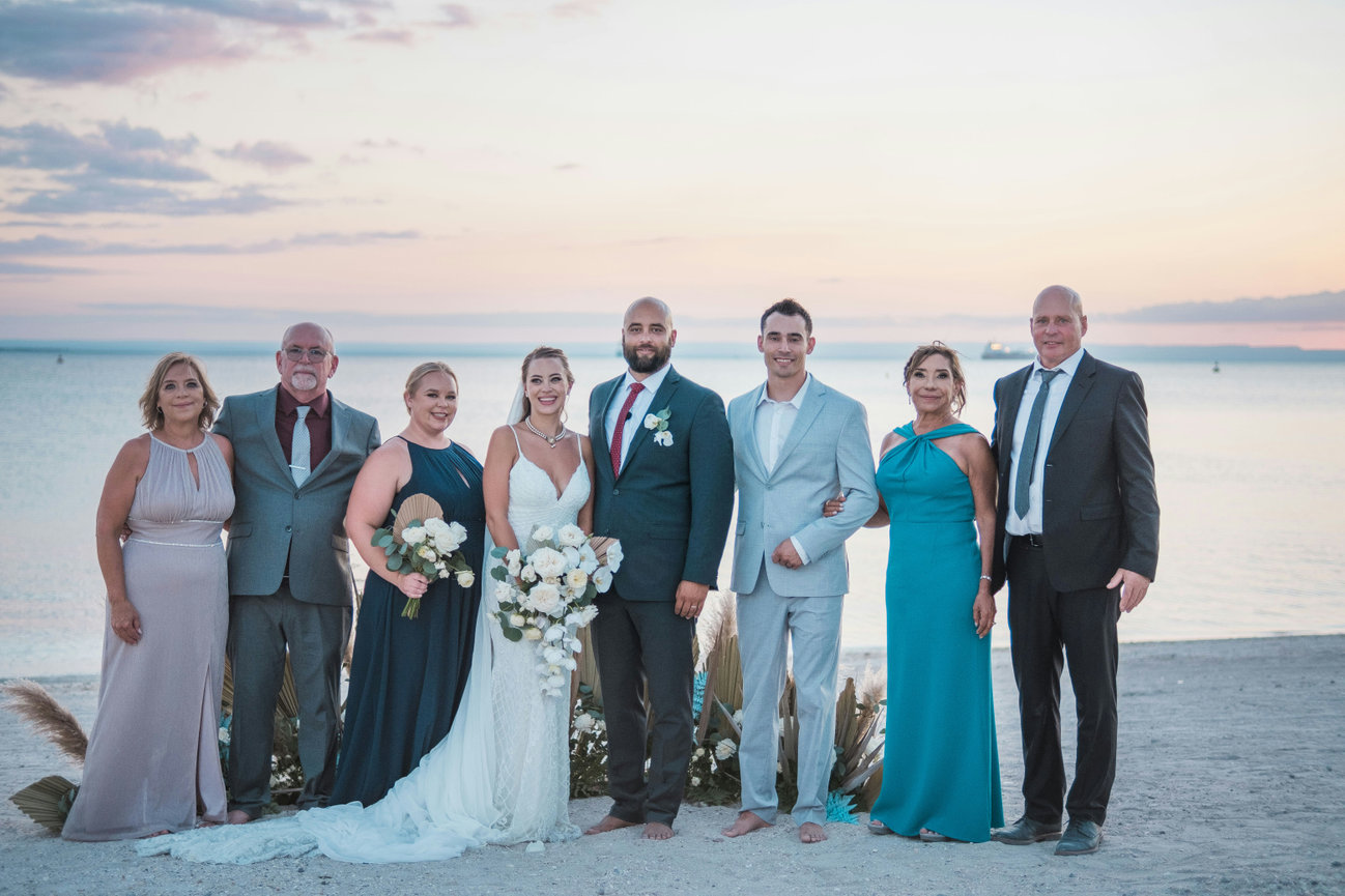 Wedding party stands together for a group portrait at sunset by the water.