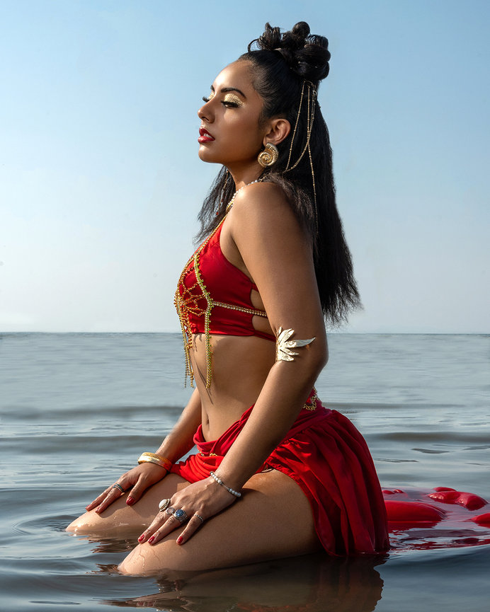 Latina model in a red outfit adorned with gold accents, kneeling gracefully in shallow water at the Great Salt Lake, Utah. Captured by Tre Nelson Photo, showcasing Latina fashion, elegance, and natural beauty.
