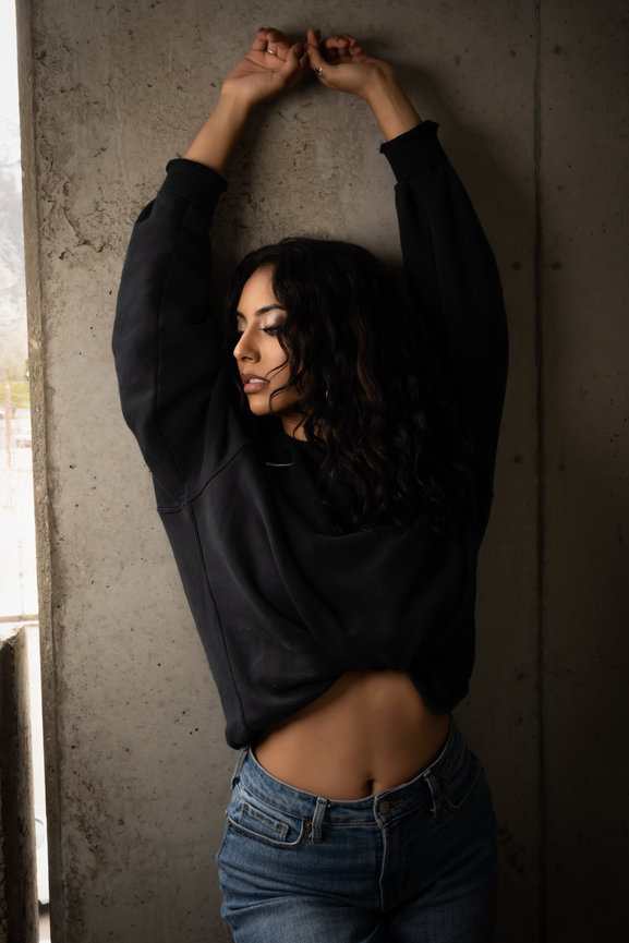 Latina model posing gracefully in a Provo, Utah parking garage, wearing a casual black sweatshirt and jeans. Captured by Tre Nelson Photo, highlighting urban fashion and natural beauty in a modern setting.