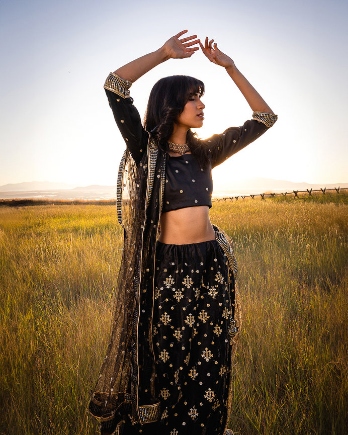 Elegant woman in traditional black and gold Pakistani attire posing gracefully in a sunlit field near Salt Lake City, Utah. Captured by Tre Nelson Photography, showcasing cultural beauty and sophistication in a serene outdoor setting.
