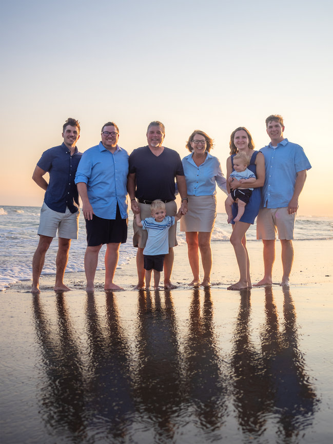 Large family stands together on shore at sunset with a water reflection.