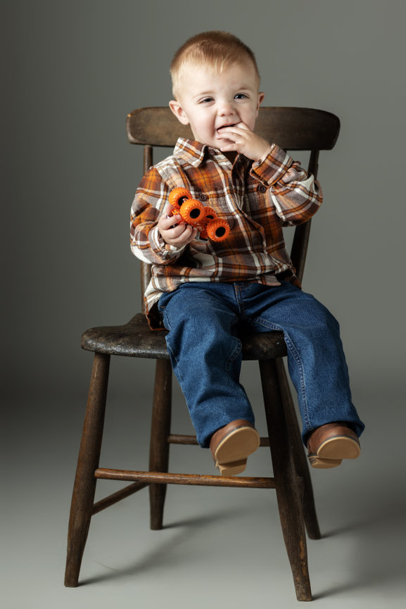 Boy holding orange toy sitting on a chair