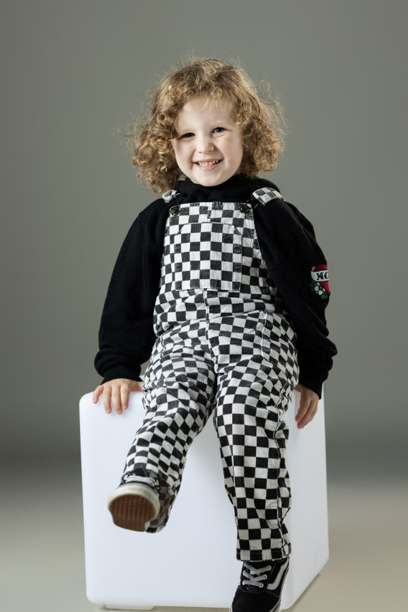 Child in checkered overalls sitting on a block