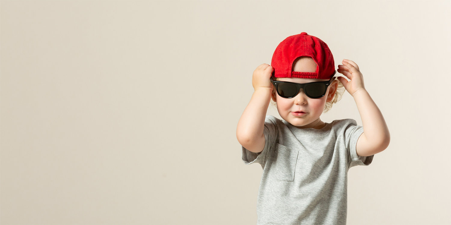 Studio portrait of a toddler wearing a red hat and sunglasses against a neutral background, photographed by a Sherman TX children’s photographer