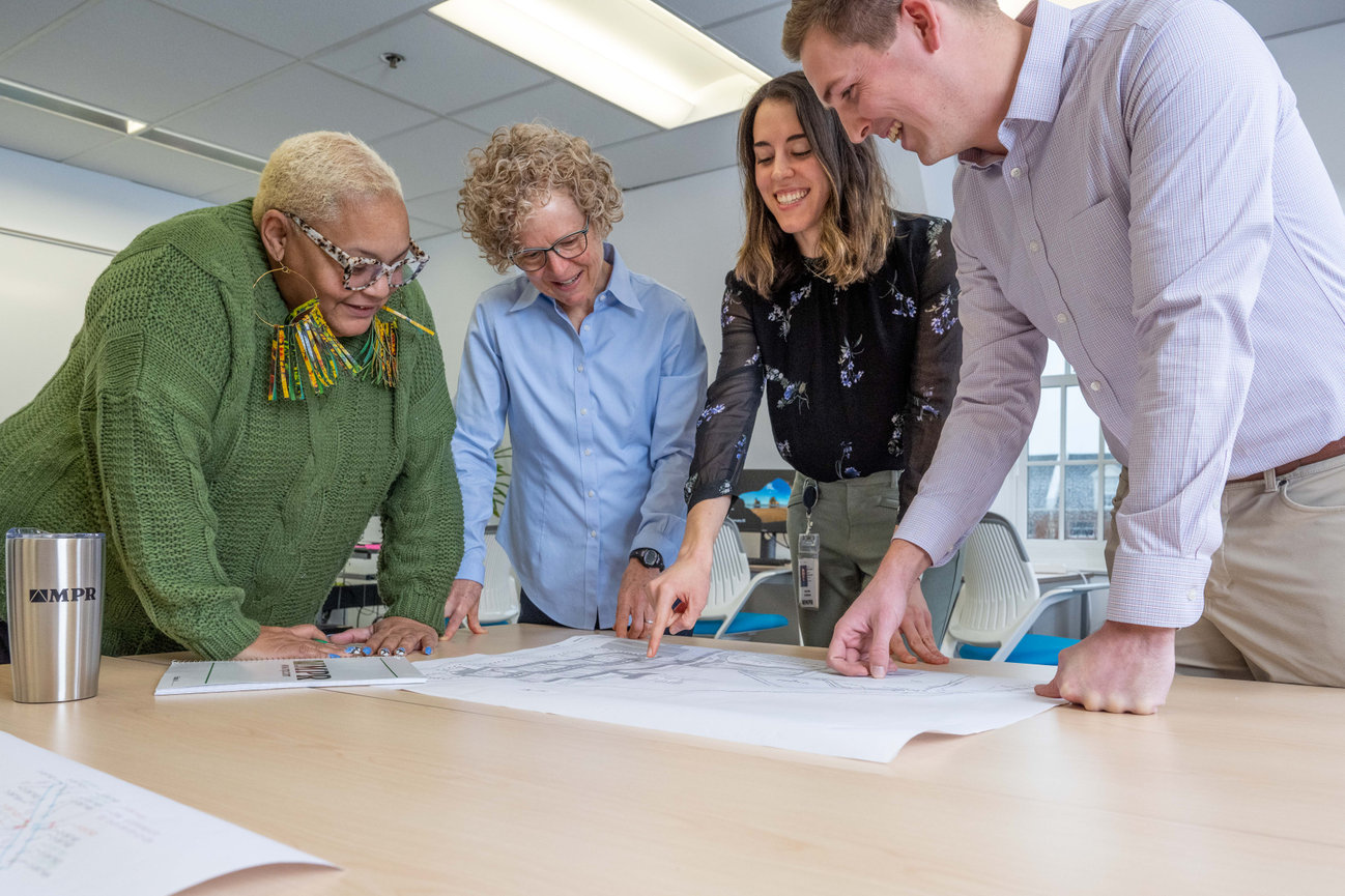 Four coworkers smiling and reviewing plans around a conference table in a bright office