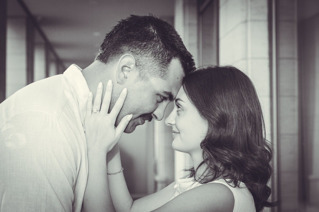 Couple touching foreheads, smiling at each other in a hallway, monochrome image.