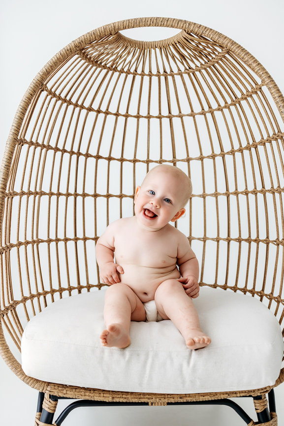 Smiling baby sitting in a large wicker chair with a white cushion.