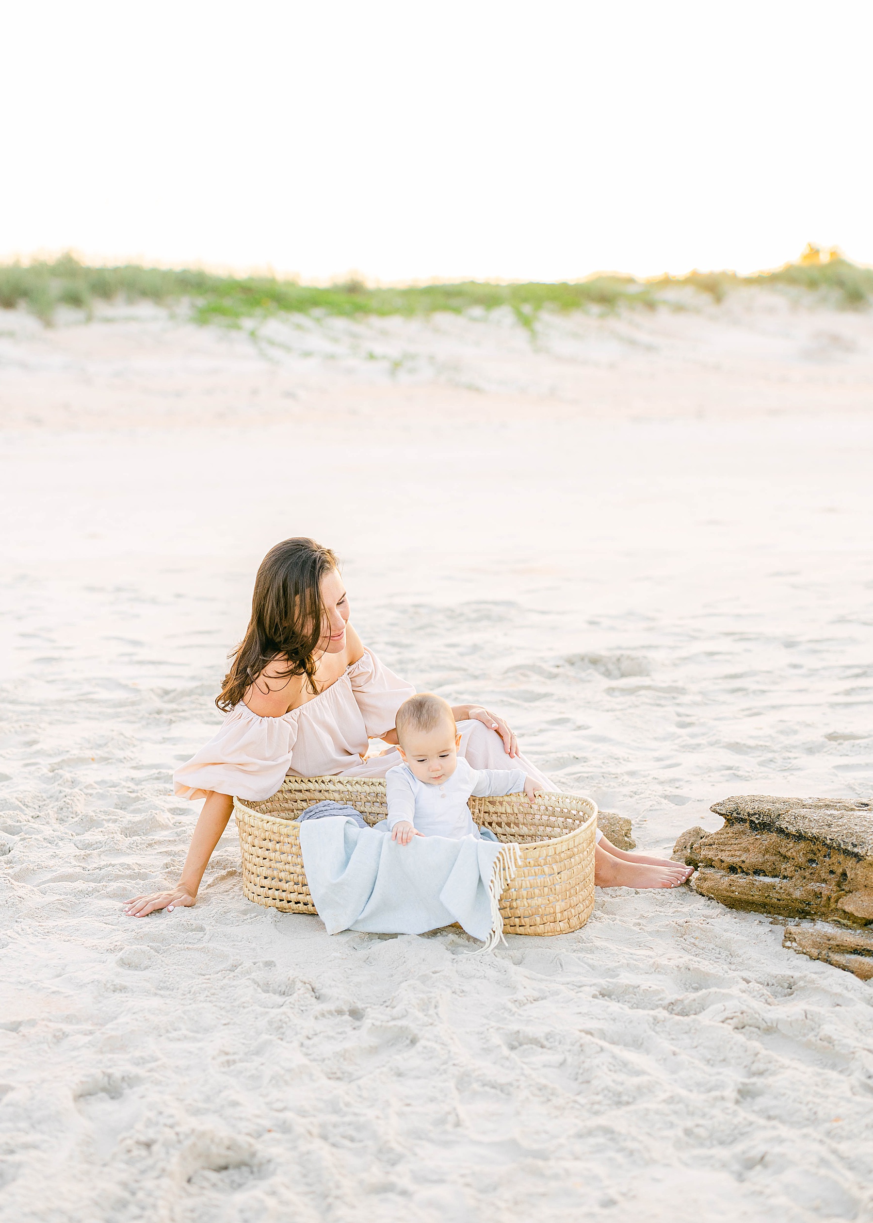 woman sitting on the beach with baby boy in basket