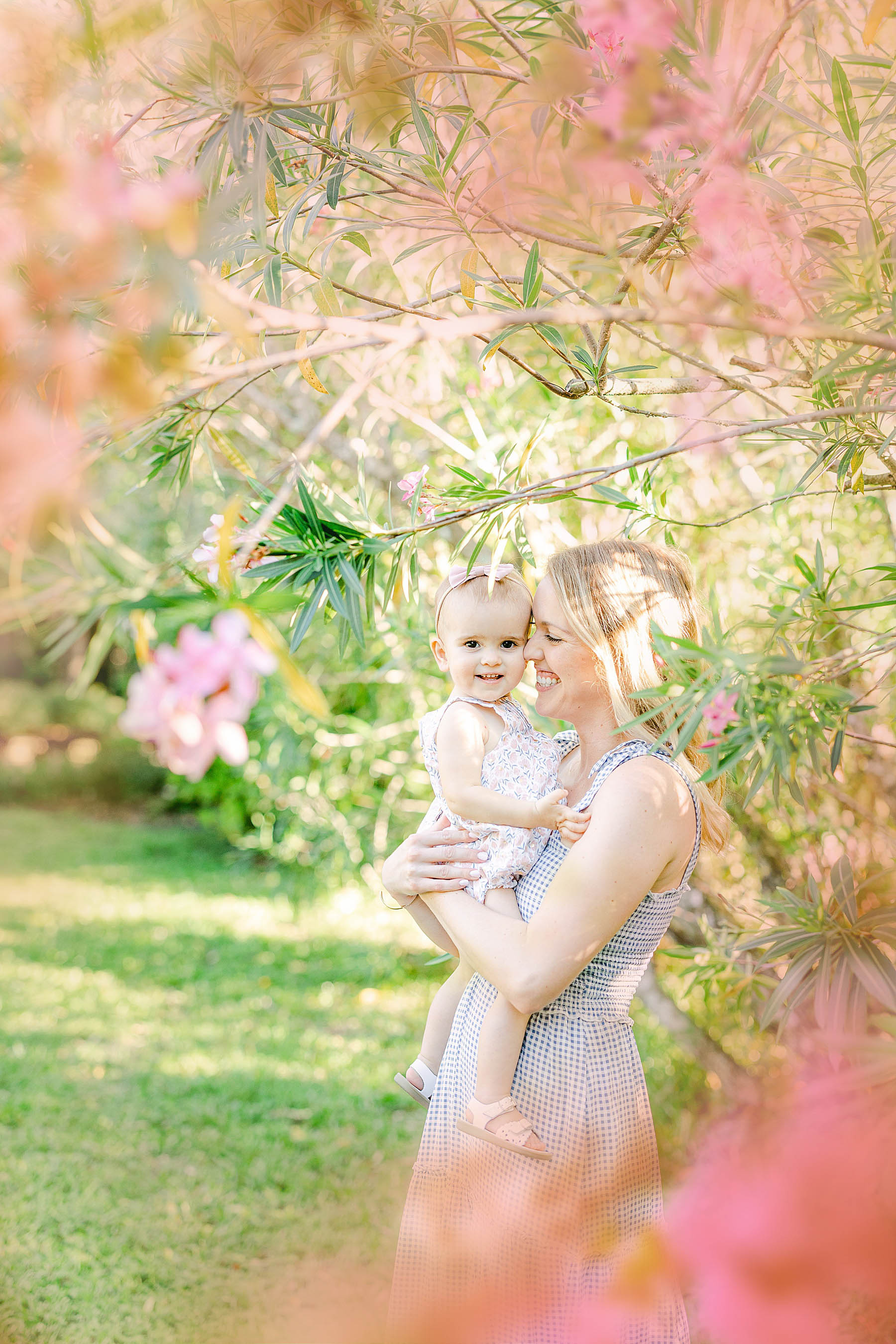 woman holding baby girl with pink flowers in spring garden