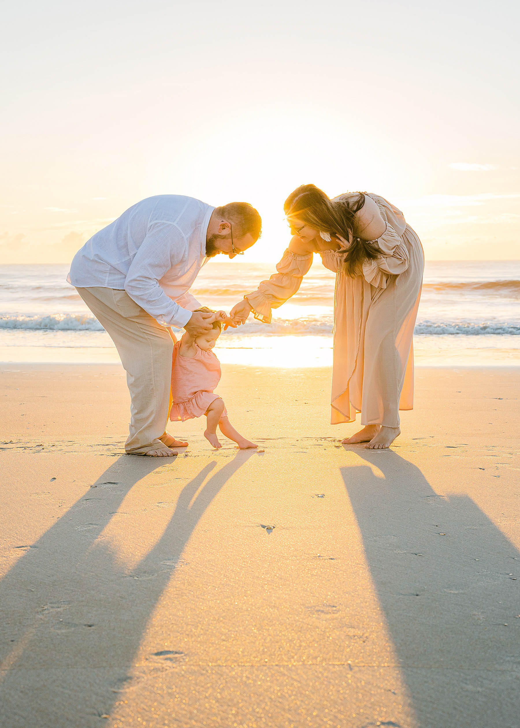 parents helping baby walk on the the beach at sunrise