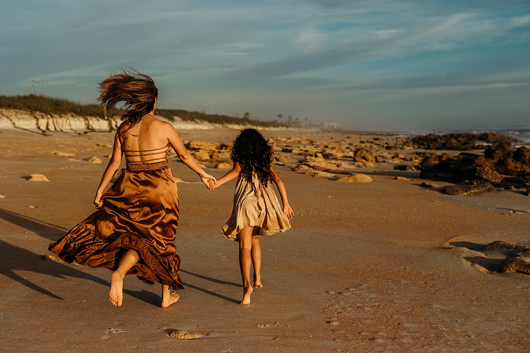woman and little girl standing on the sand of the beach at sunrise