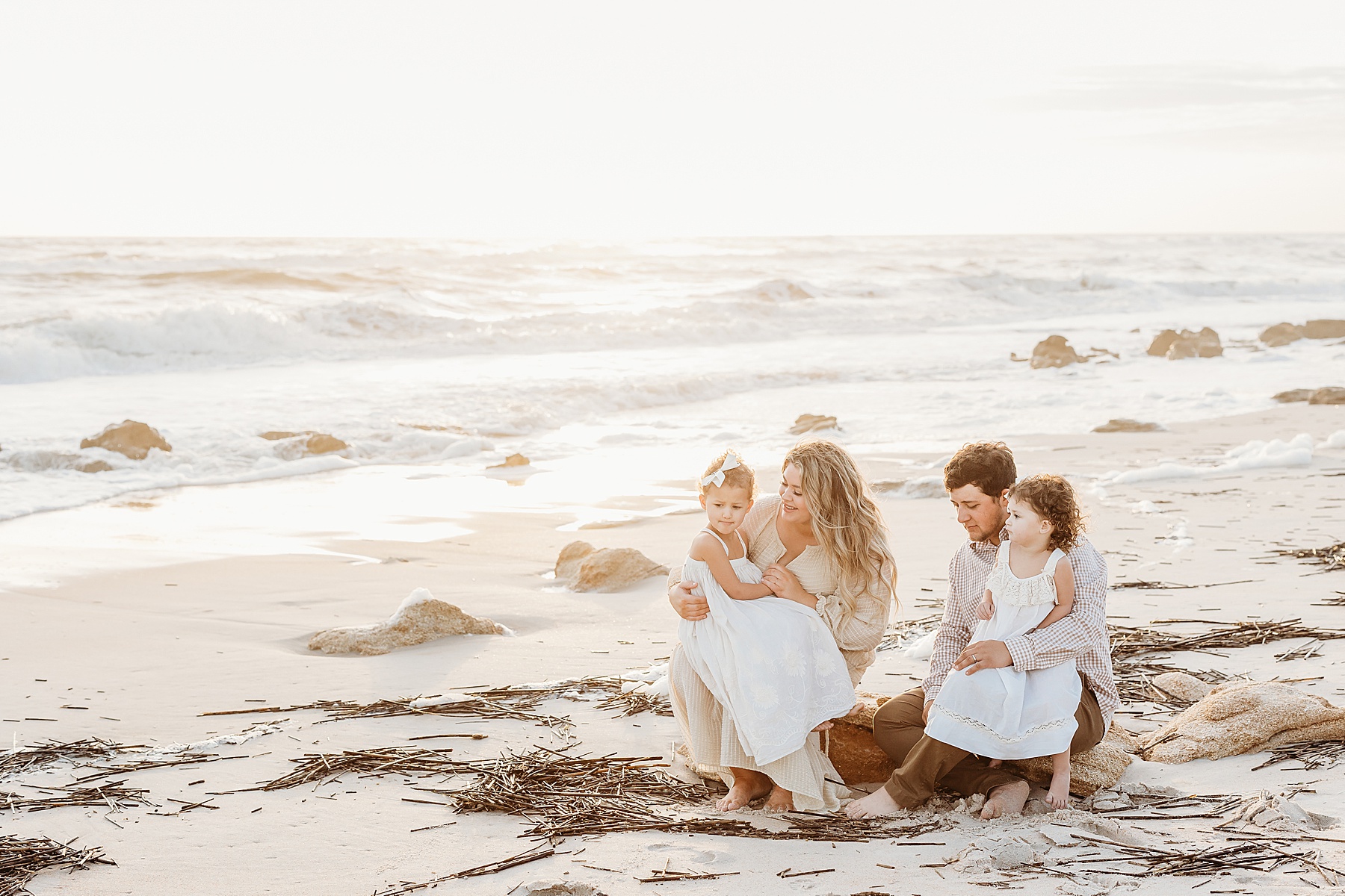 family sitting on a rock at the beach at sunrise wearing neutral colors