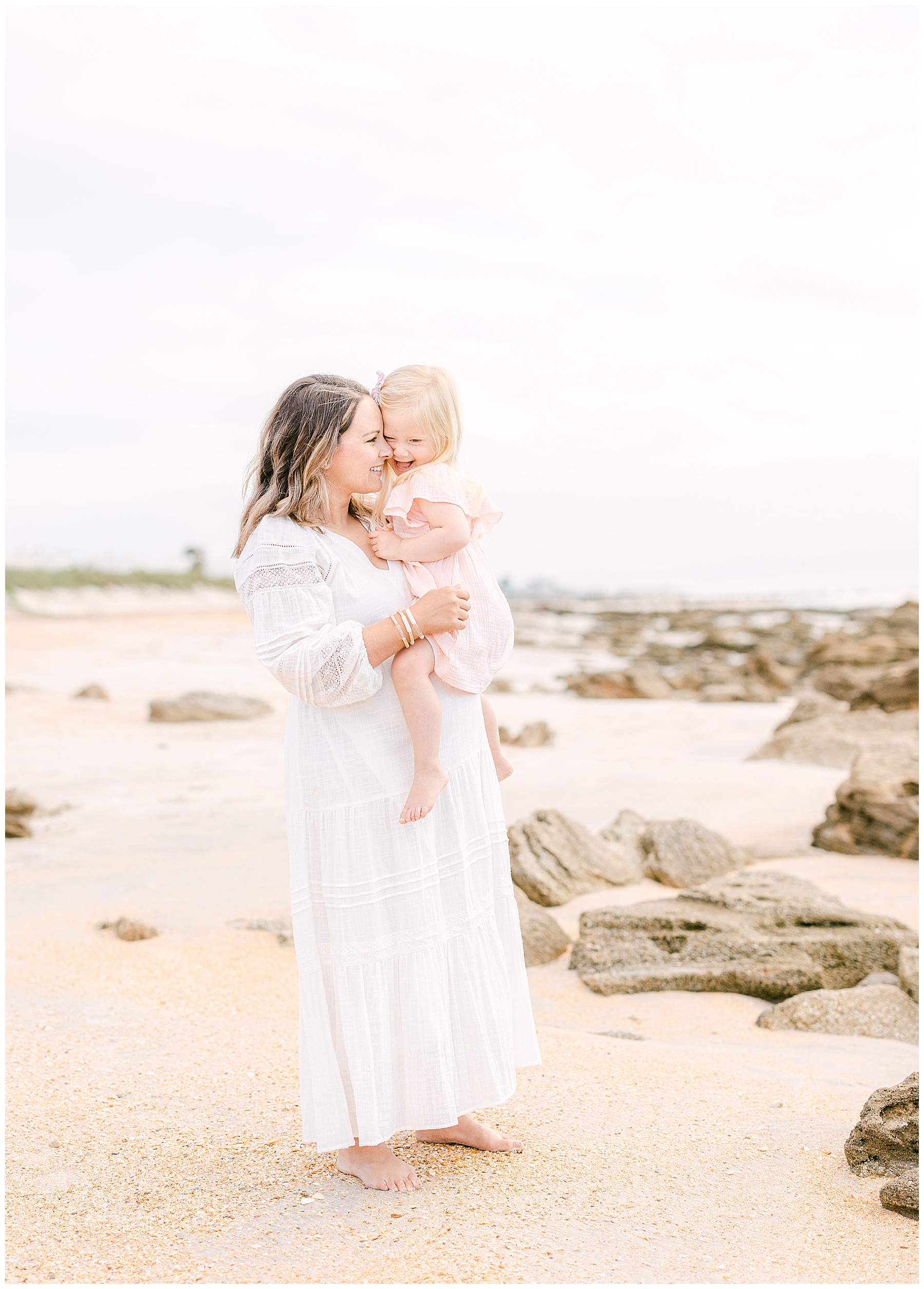 mom holding baby girl in pink dress with rocks on the beach in saint augustine florida