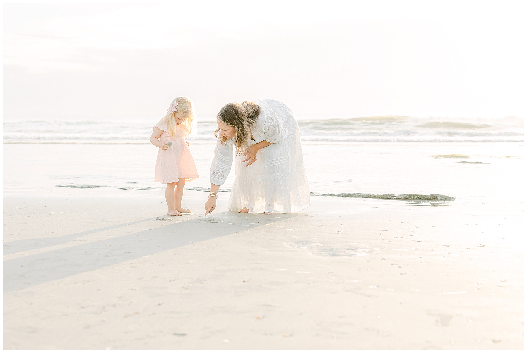 woman in white dress on the beach at sunrise showing little girl shells