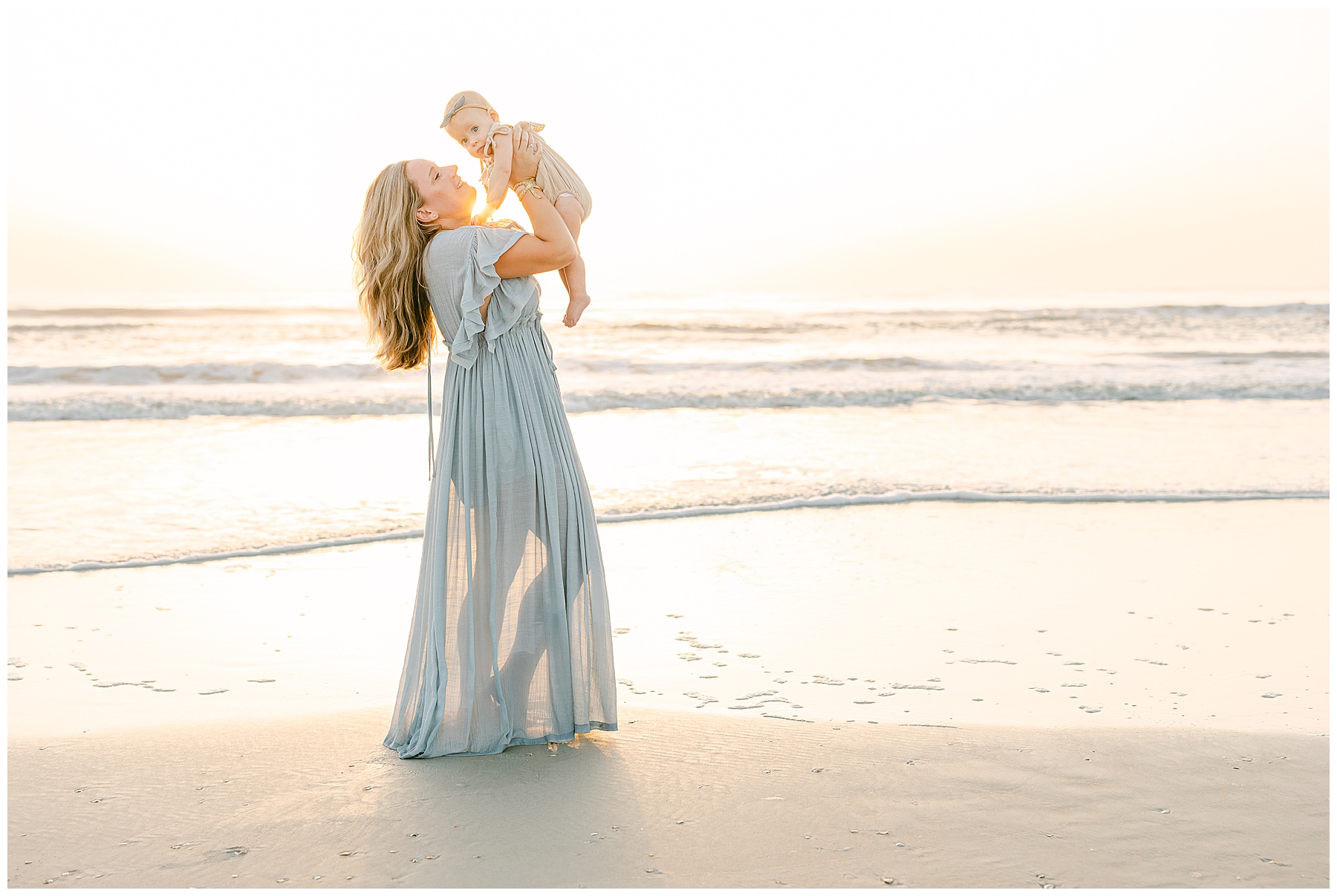 woman in sage green maxi dress holding baby girl up in the air on the beach at sunrise in saint augustine florida