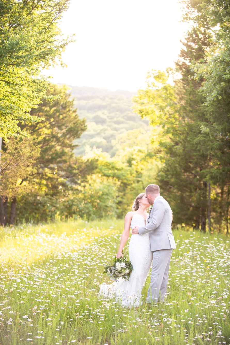 Groom dipping bride while they stand in a field of daisies at sunset.