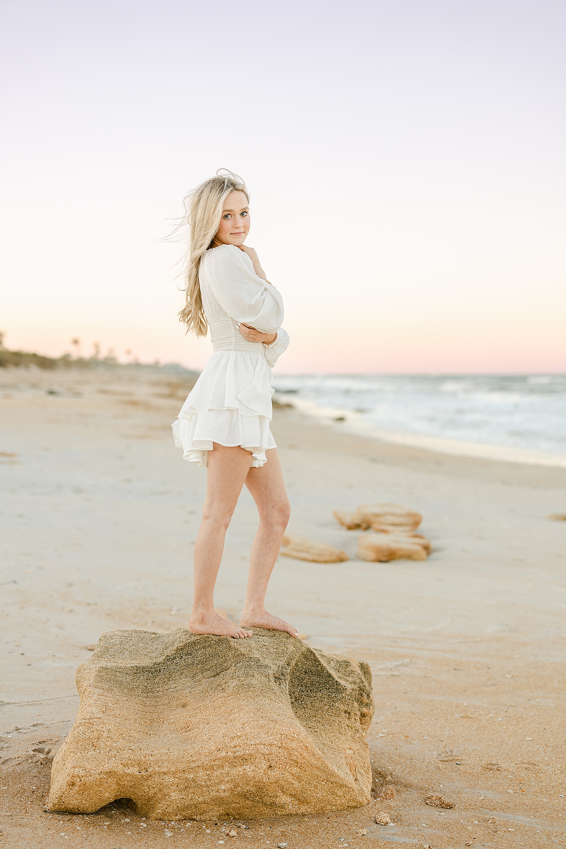 blonde girl standing on coquina rocks during a pastel sunset in Saint Augustine Beach Florida