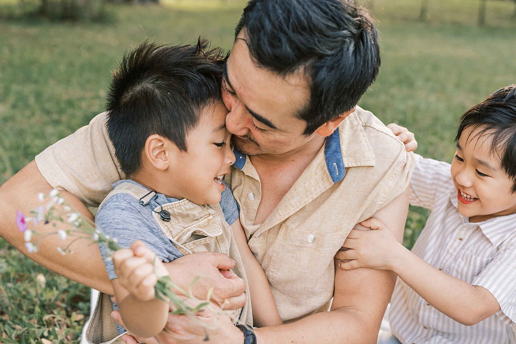 man playing with little boys in a flower field laughing with family at newborn session