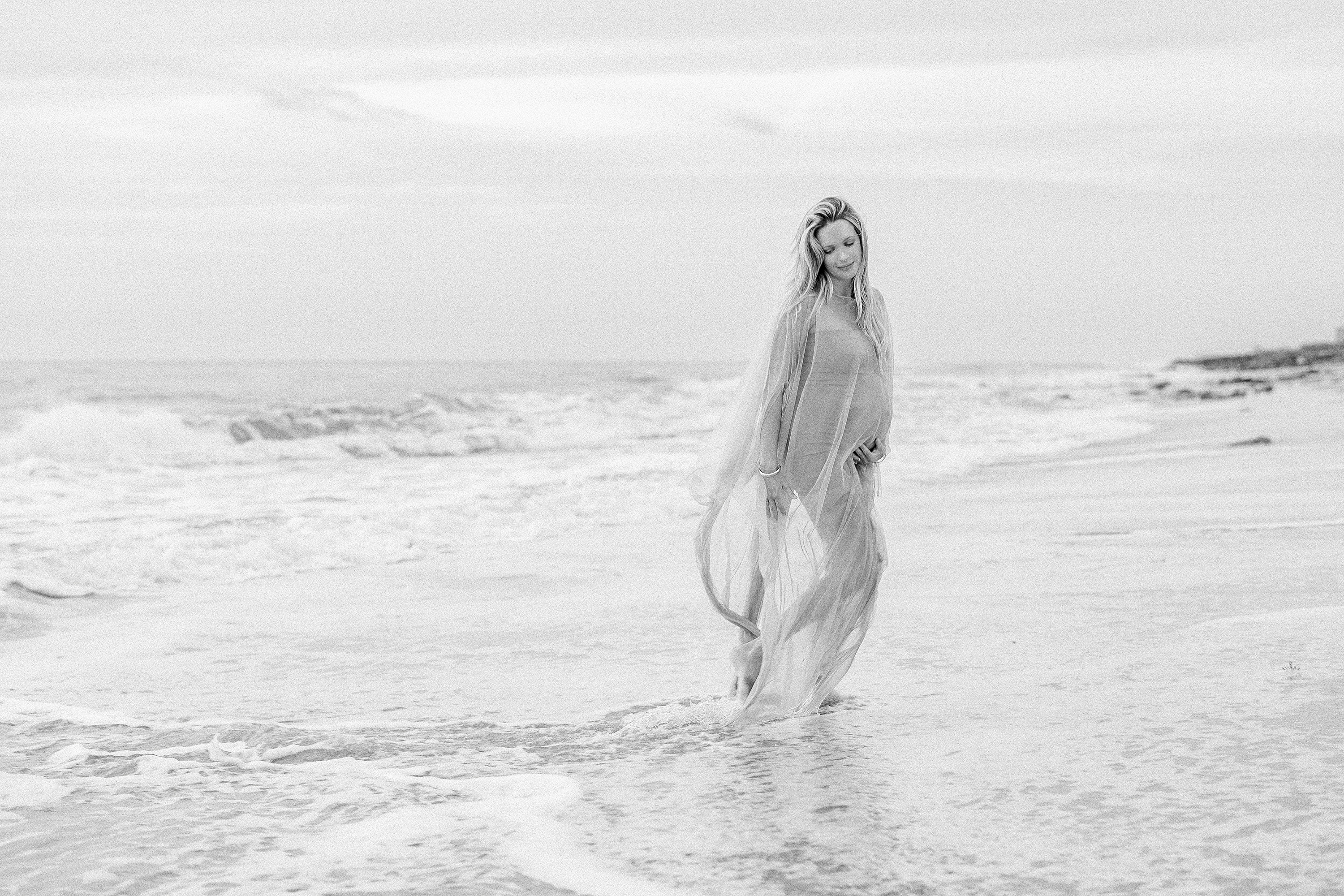 fine art black and white maternity portrait of blond woman at the beach at sunrise