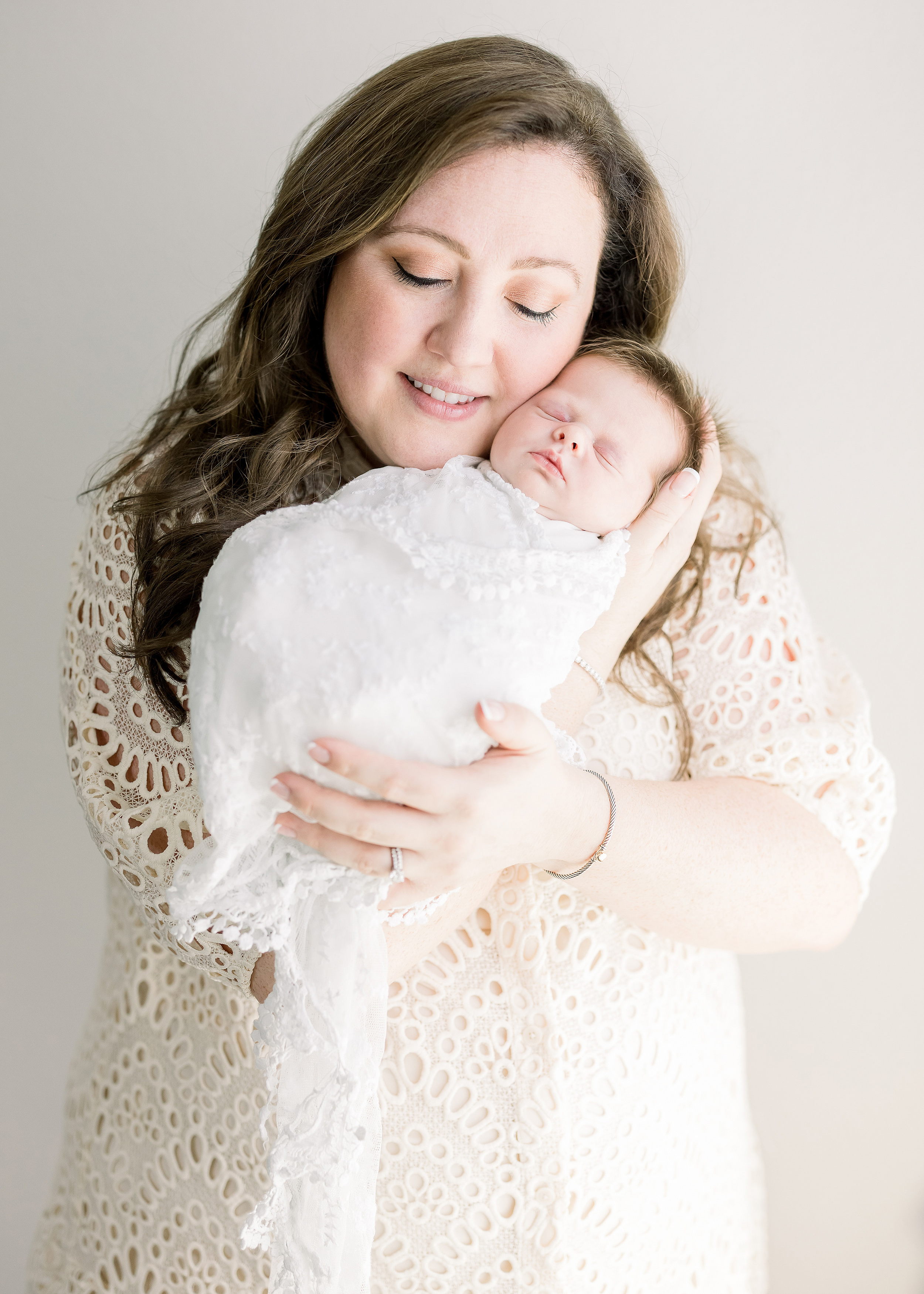 woman in cream lace dress holding newborn baby girl wrapped in white swaddle