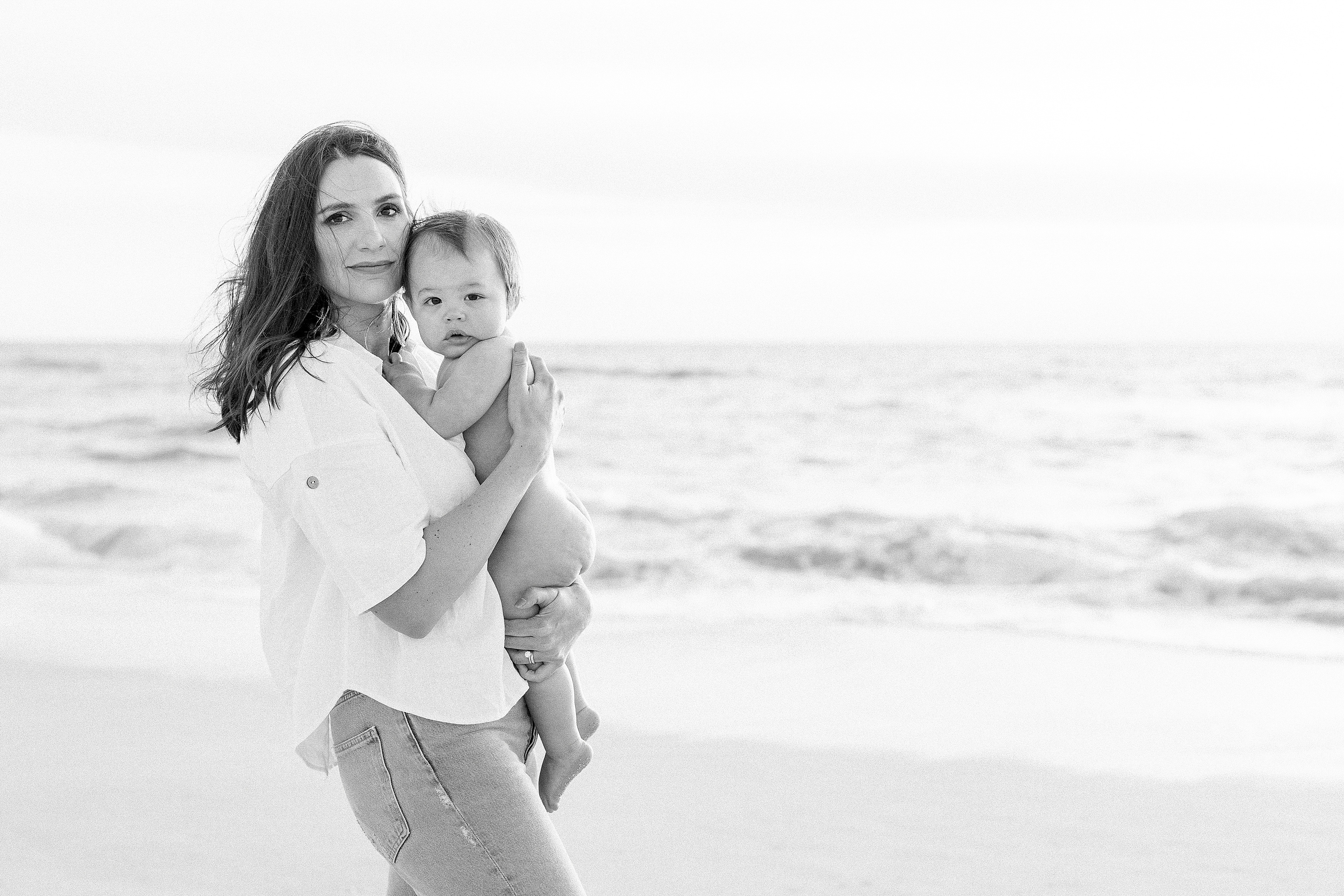 black and white photography of woman holding baby boy at the beach at sunrise