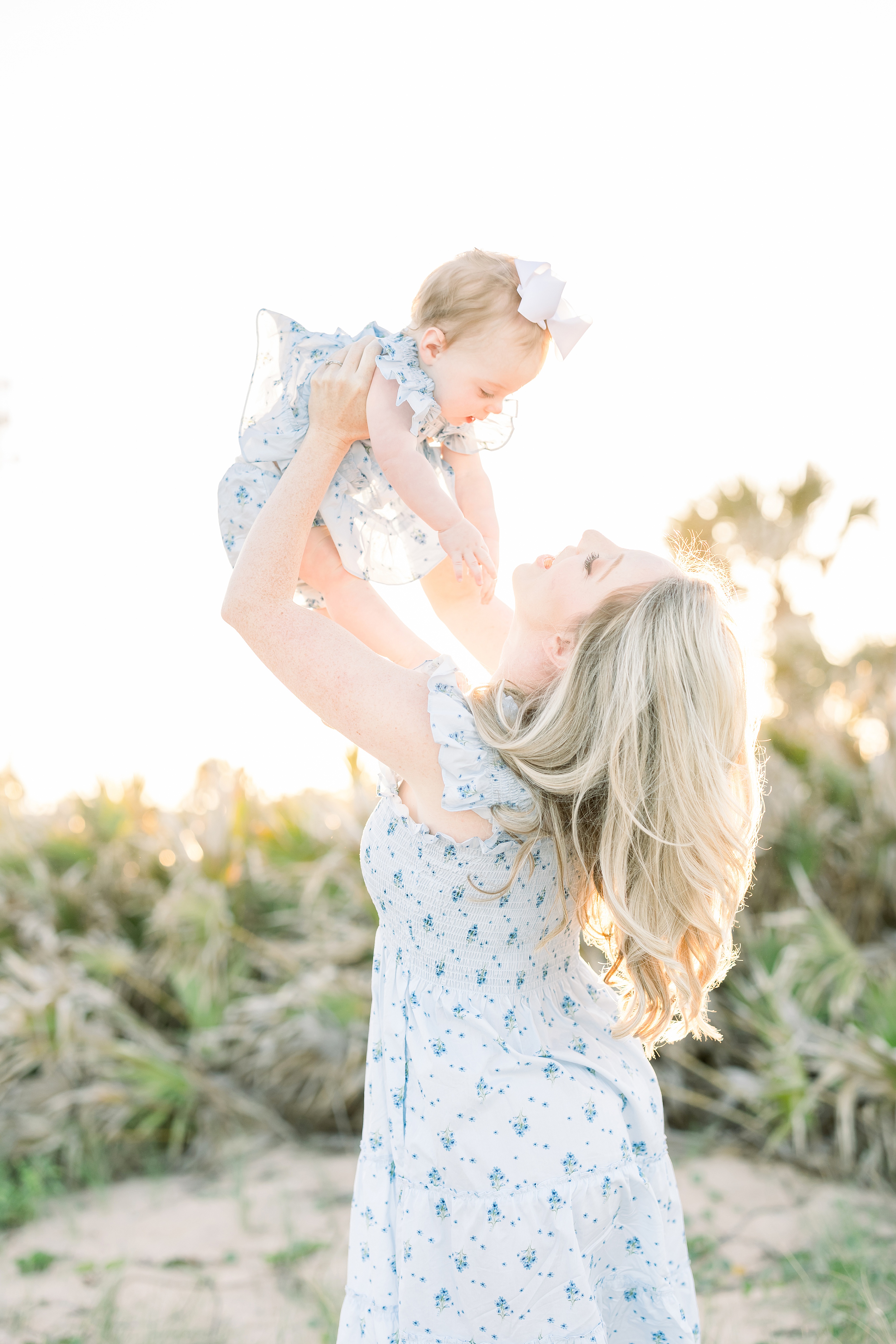 blonde-haired woman in blue and white floral nap dress at the beach at sunset