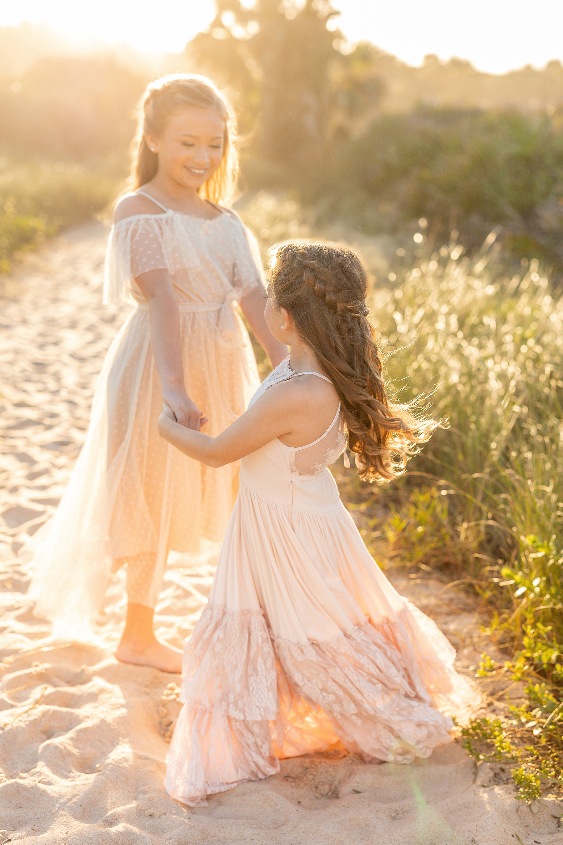 Two little girls twirl together on a light filled evening at sunset on the sand.