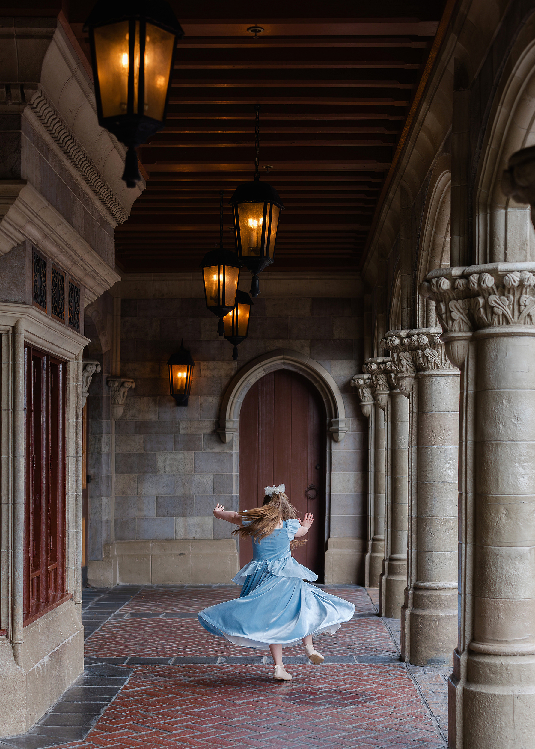 A little girl in a blue dress twirls on the side of Cinderella's Castle at the Magic Kingdom.