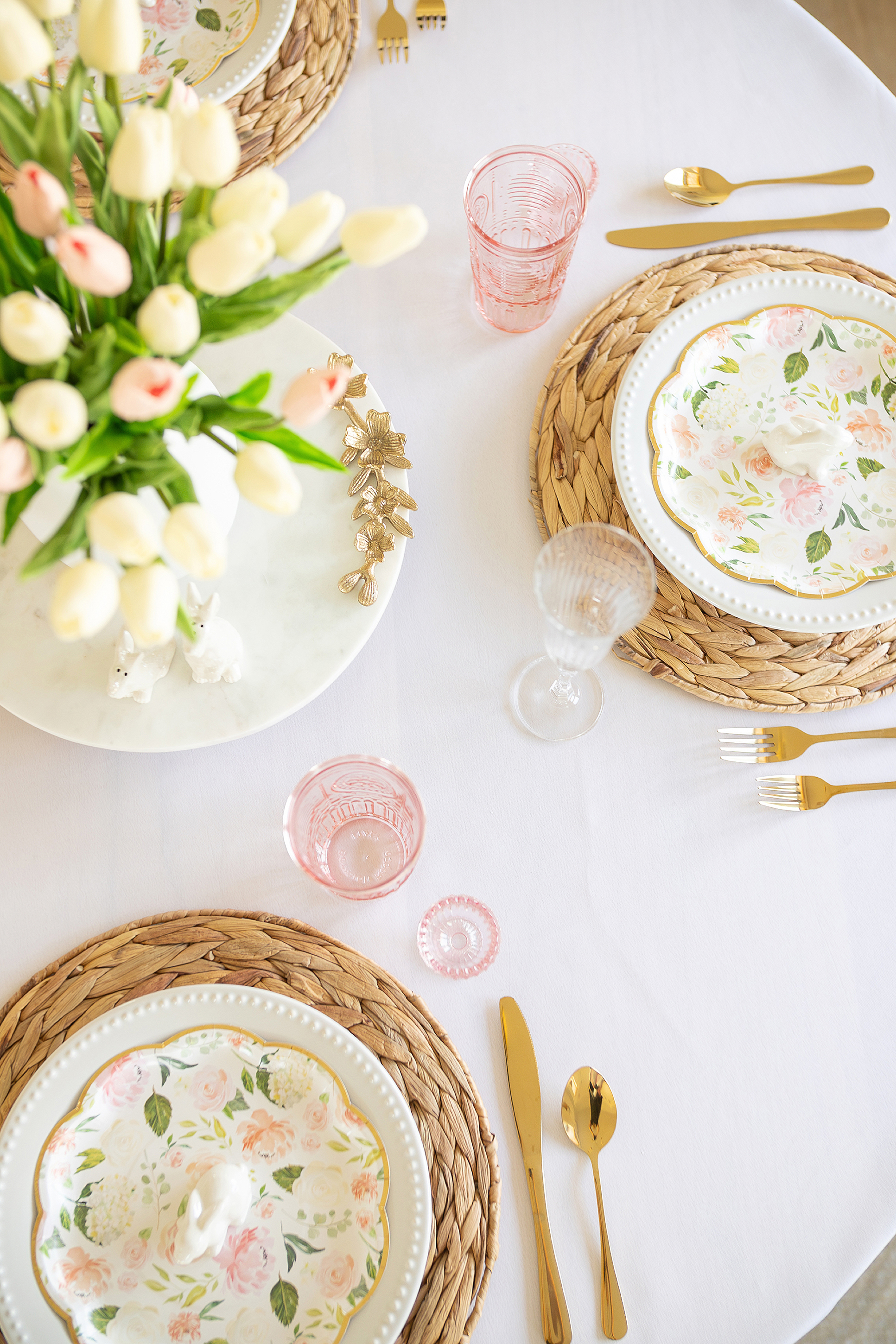 A pink and white pastel table set for Easter with tulips and pink glasses.