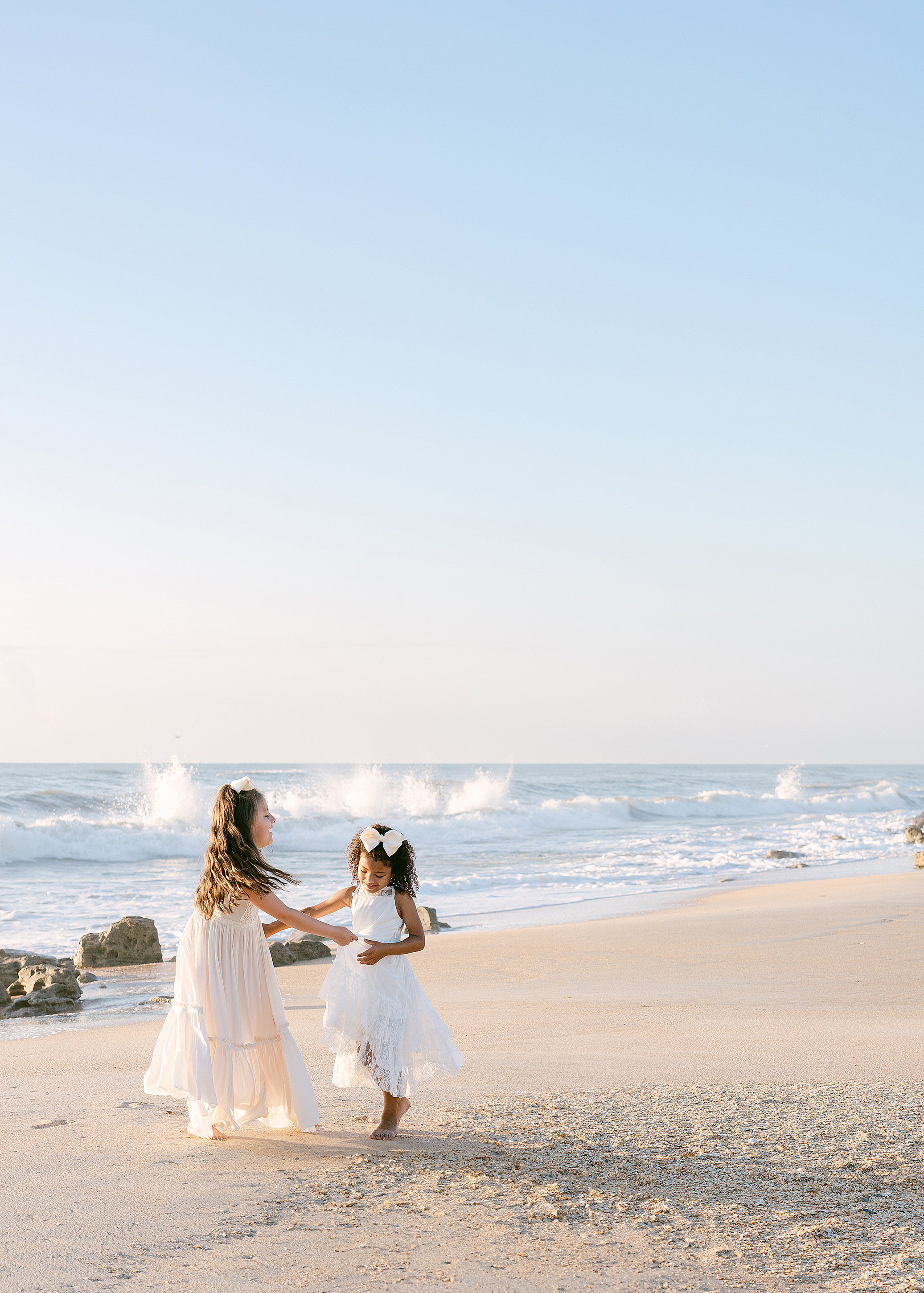 Two little girls twirl together on Saint Augustine Beach at sunrise.