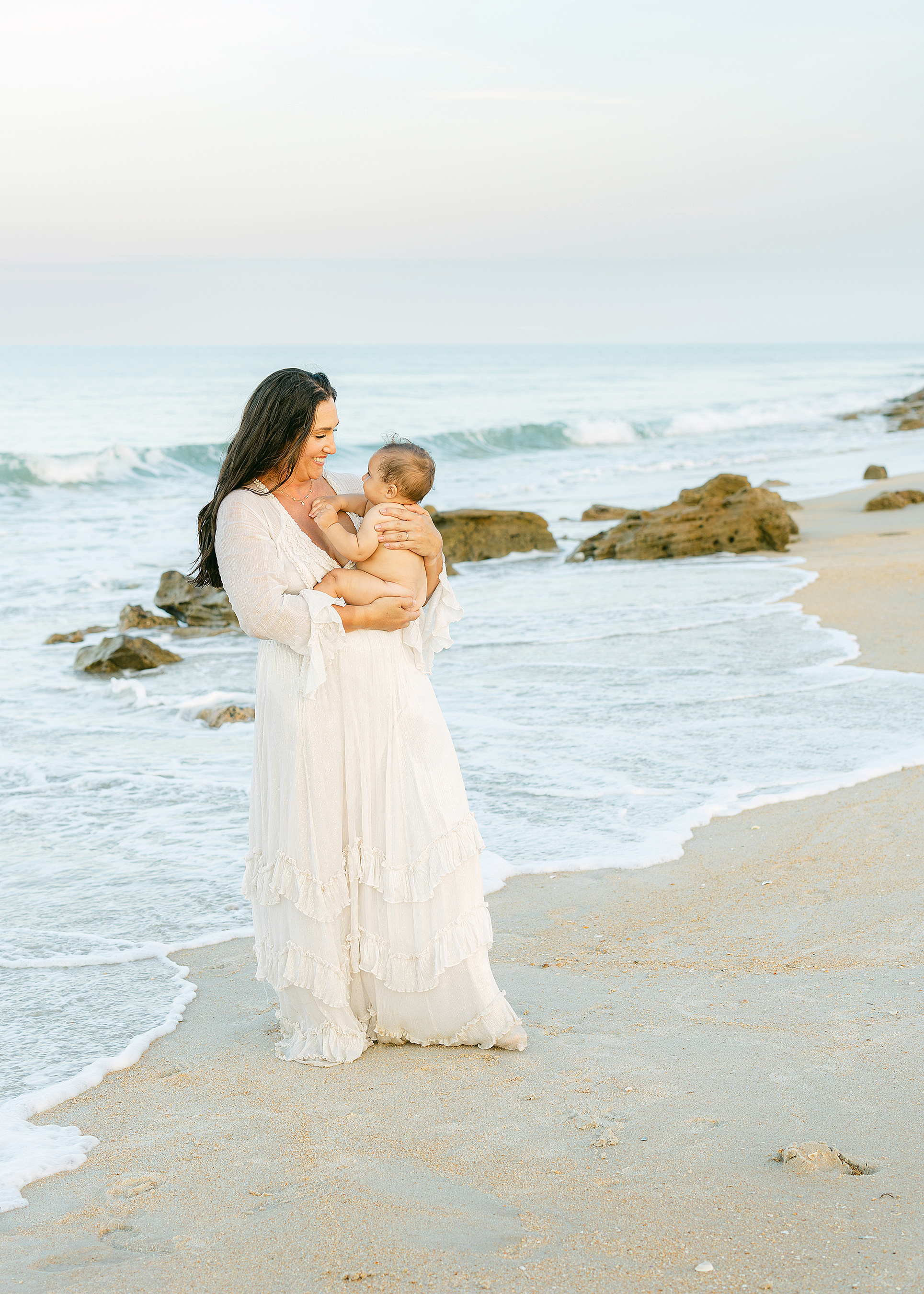 A pastel, colorful sunset motherhood portait of a woman and her baby boy on Saint Augustine Beach.