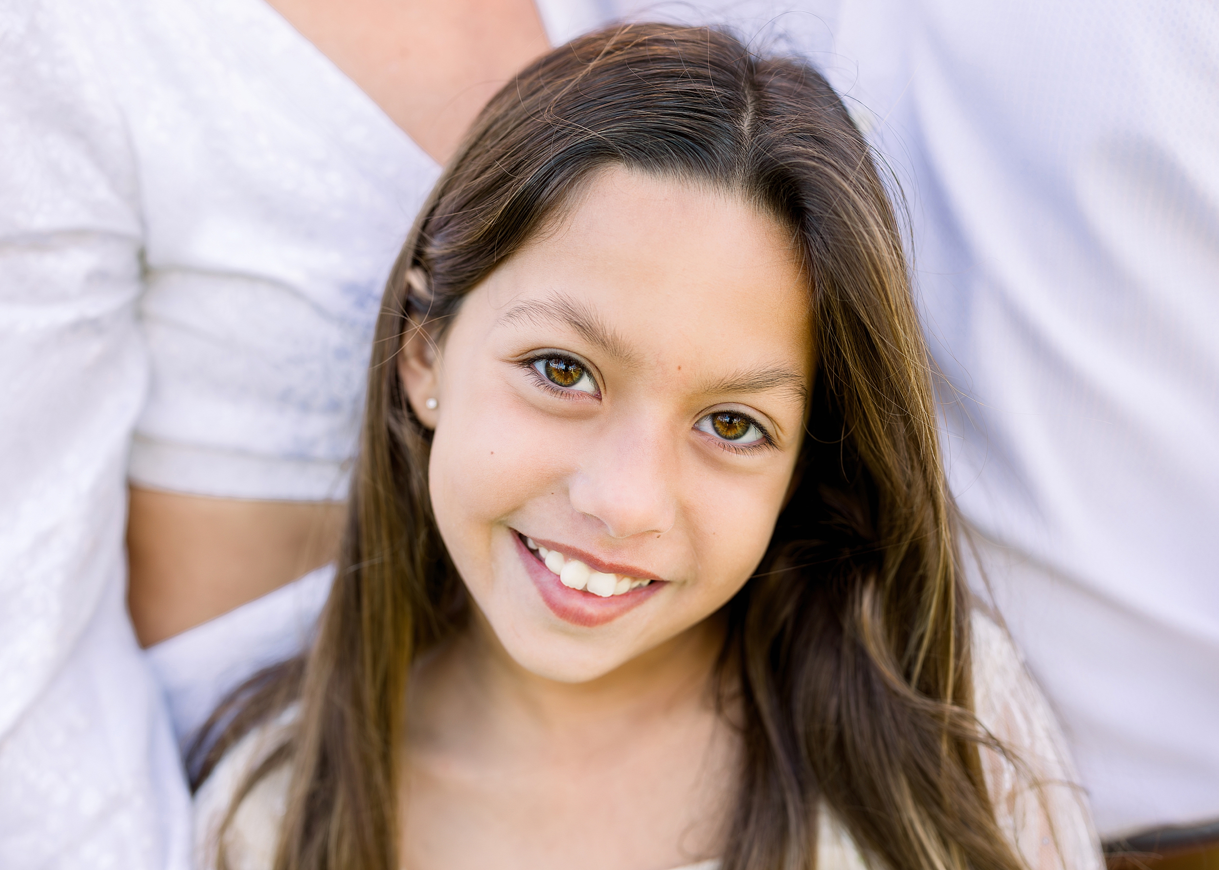 A close up portrait of a little girl in a cream dress in the park.