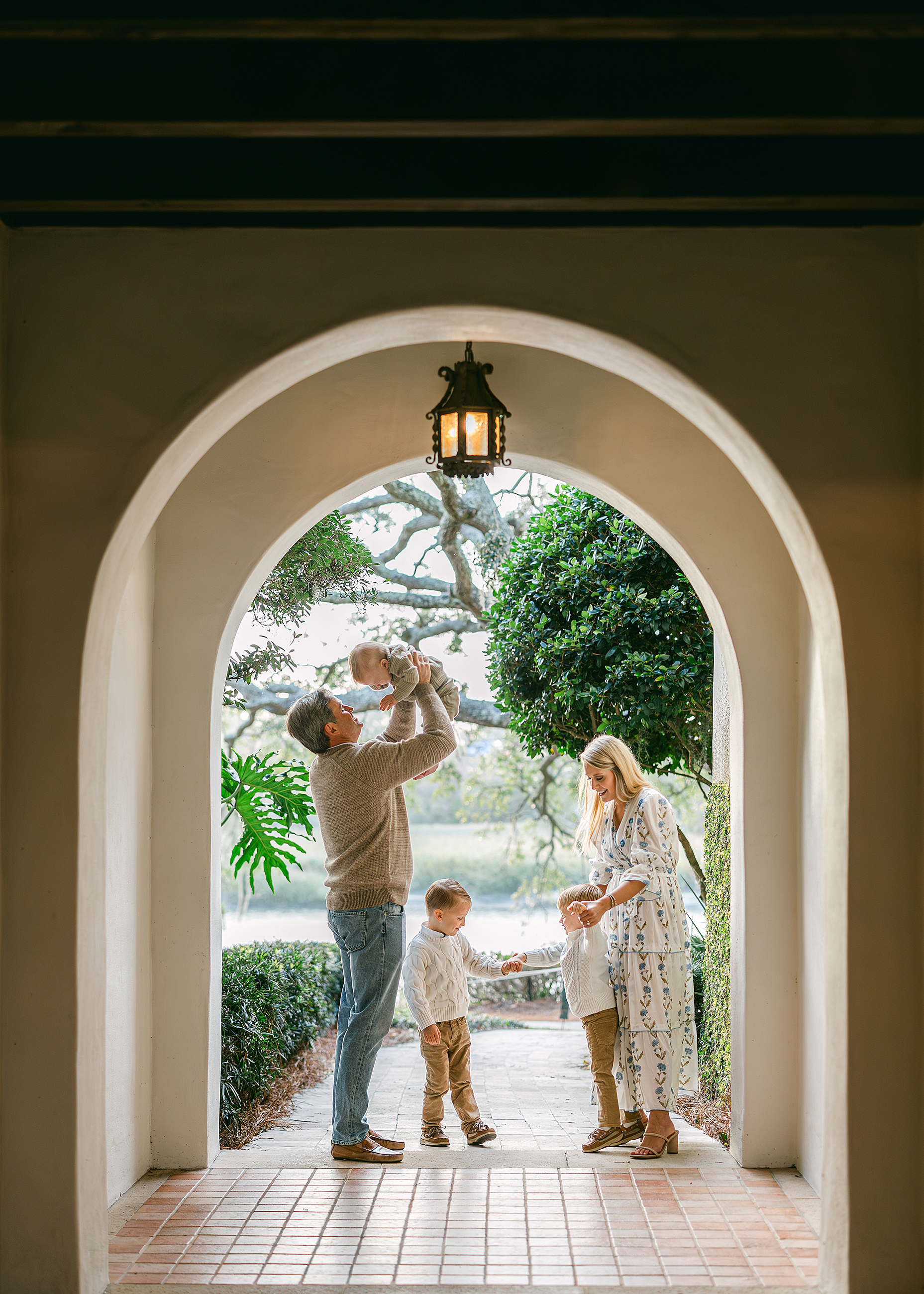 A family stands in an outdoor hallway of the Cloister along the marsh while playing together.