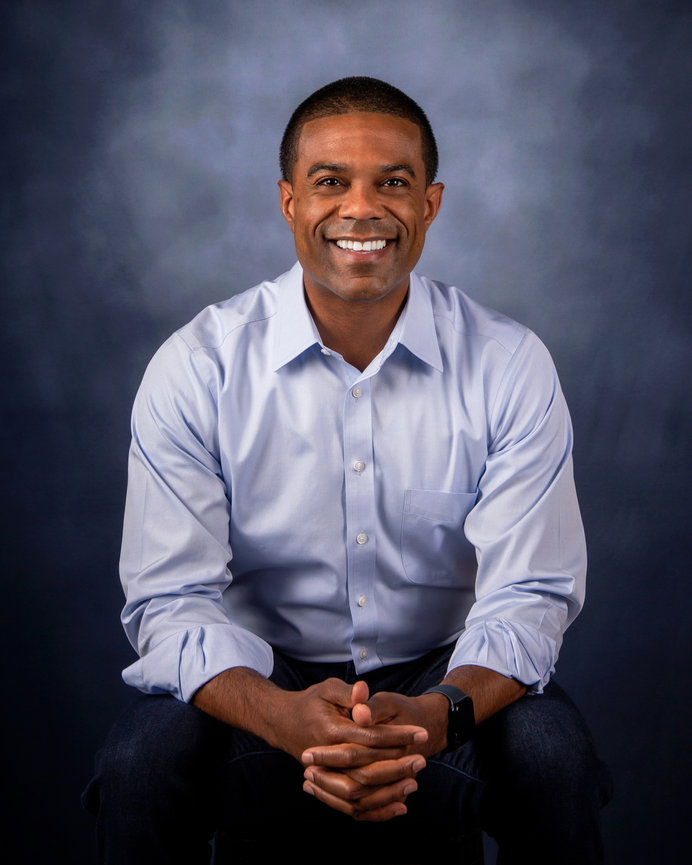 Smiling person in a light blue shirt sitting against a dark blue background.