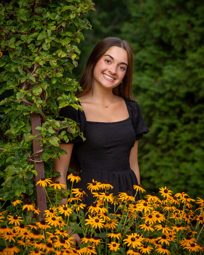 Woman in a black dress smiling, surrounded by yellow flowers and greenery.